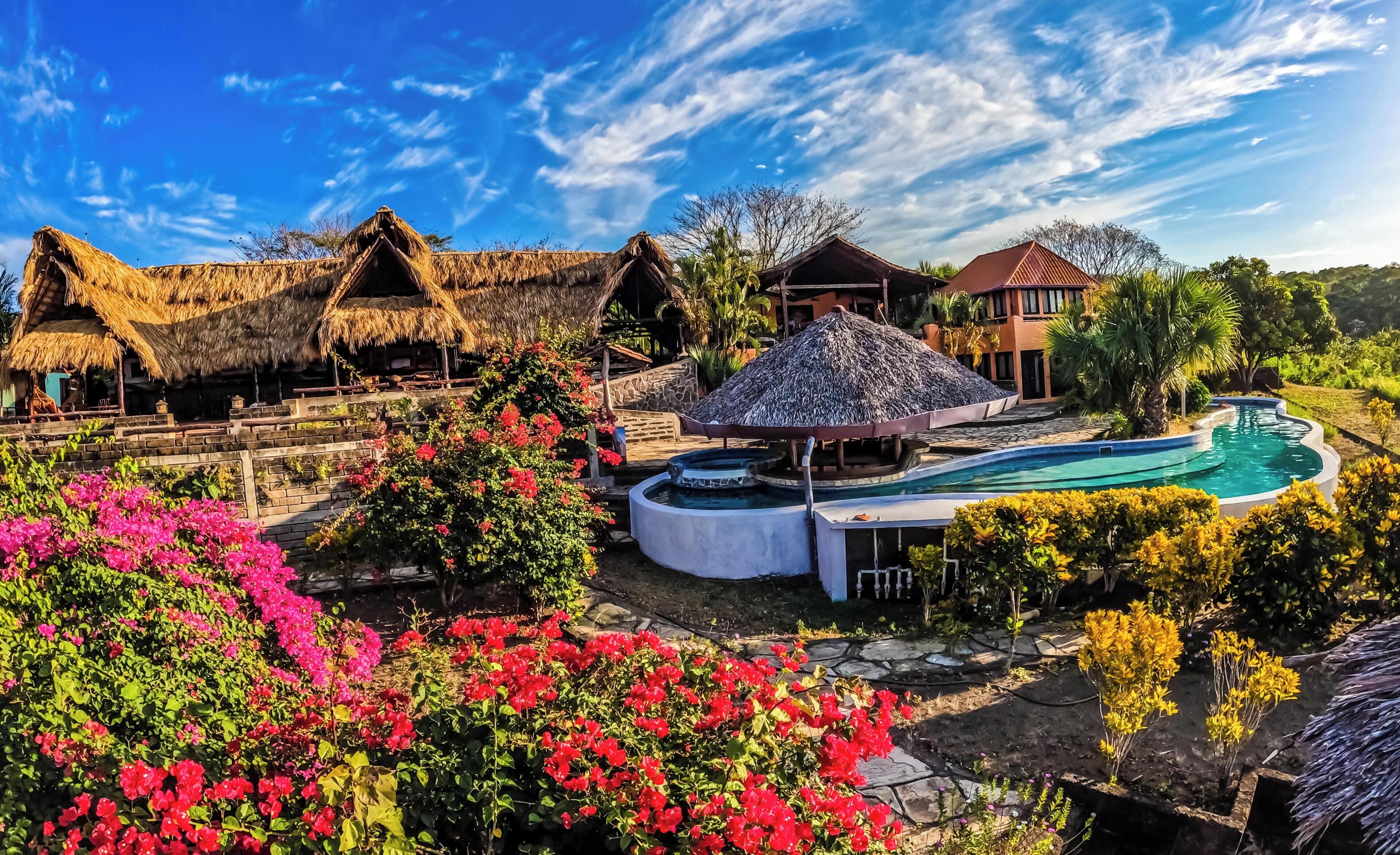Un complexe hôtelier doté de bungalows aux toits de chaume, d’une piscine et de jardins luxuriants.