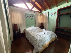 A bedroom with a bed, curtains, a chair, a TV, and a ceiling fan.