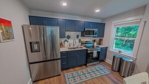 A modern kitchen with stainless steel appliances, blue cabinets, and a window with a view of greenery. - Charming Coastal Oasis with Heated Pool in Kitty Hawk, NC (Kitty Hawk)