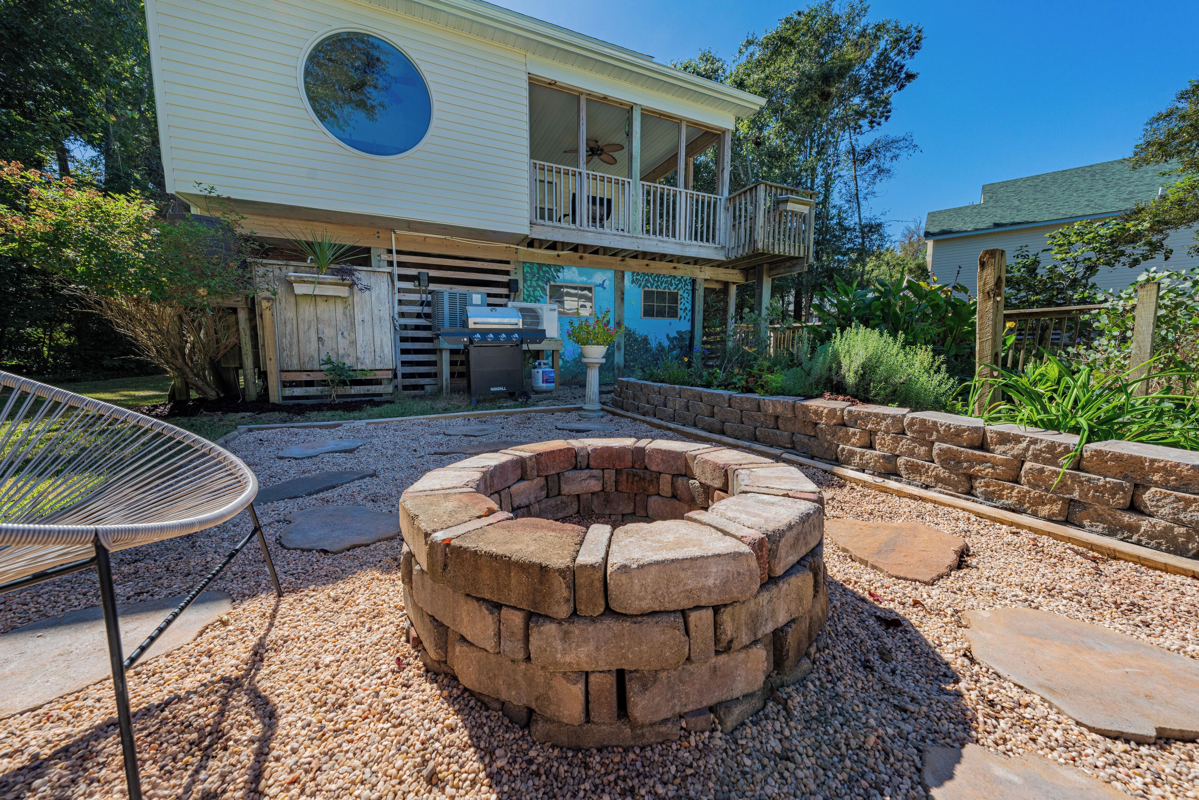 A house with a circular fire pit, a covered outdoor seating area, and a large window overlooking the yard.