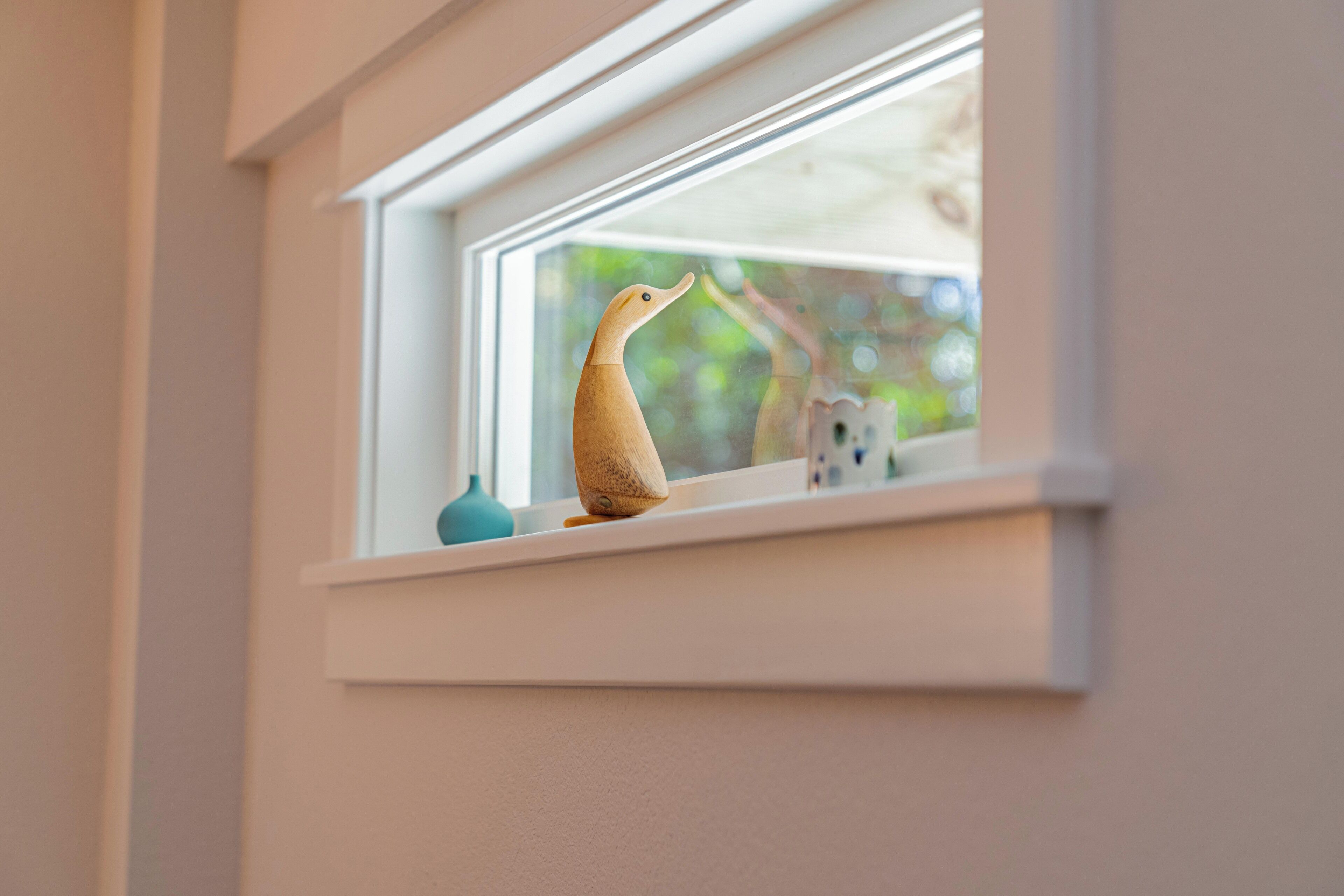 Eine Fensterbank mit einer hölzernen Entenfigur und einer kleinen Vase.
