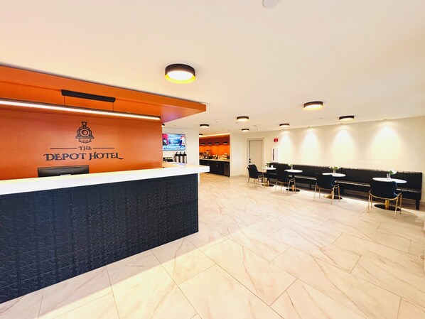 A hotel reception area with a modern design, featuring a reception desk, seating area, and a television screen.