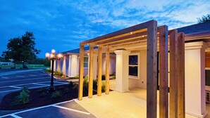 A covered outdoor area with a wooden pergola structure, a parking lot, and a building in the background. - The Depot Hotel (Taylor)