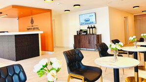 A hotel reception area with a reception desk, black leather chairs, round tables with vases of flowers, and a television screen on the wall. - The Depot Hotel (Taylor)