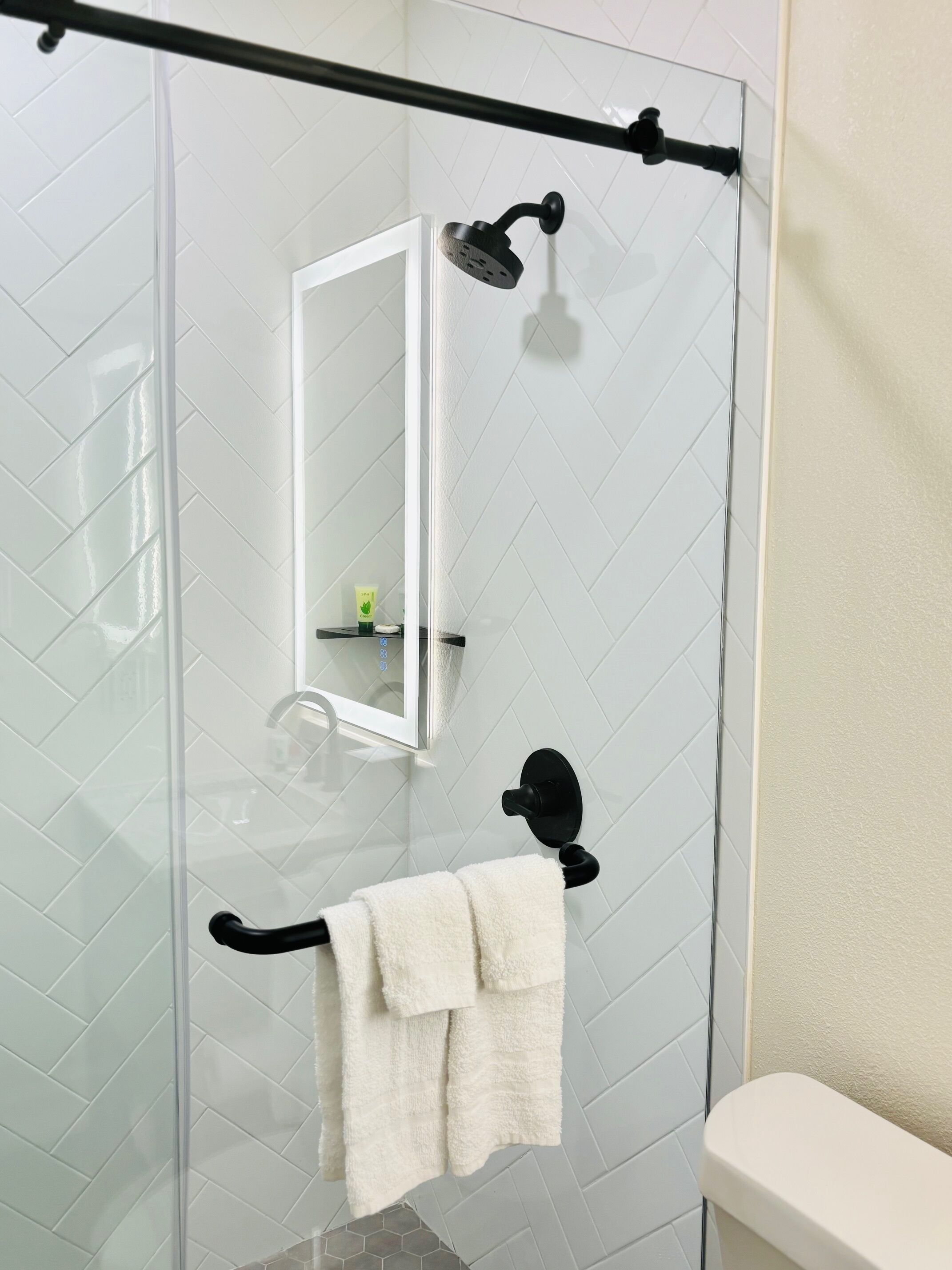 A bathroom with a glass shower enclosure, a white toilet, and a towel rack with a white towel.