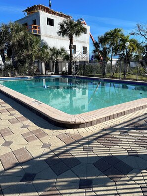 A swimming pool with a tiled deck, surrounded by palm trees and a fenced area.