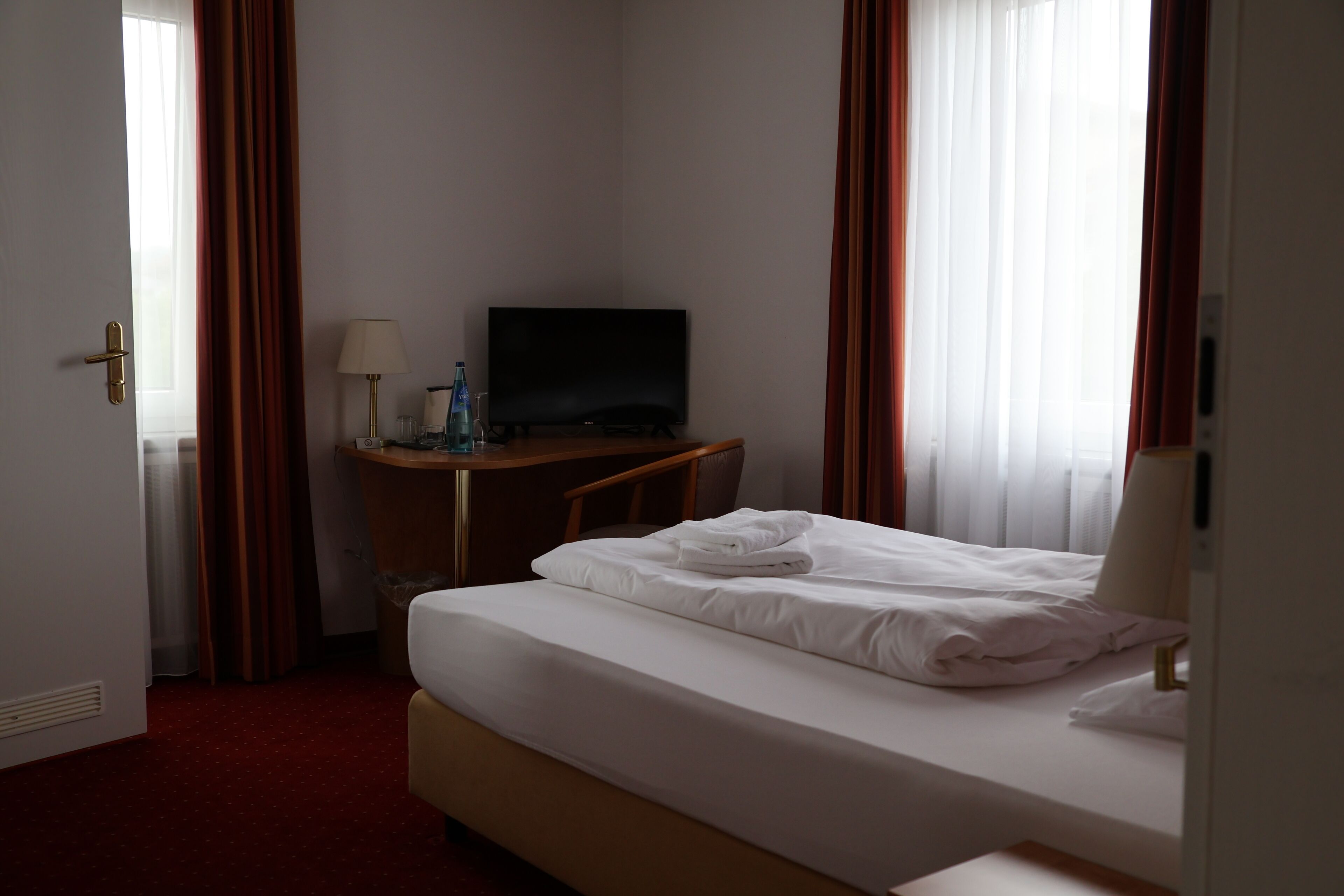 A hotel room with a bed, a desk, a television, and curtains.
