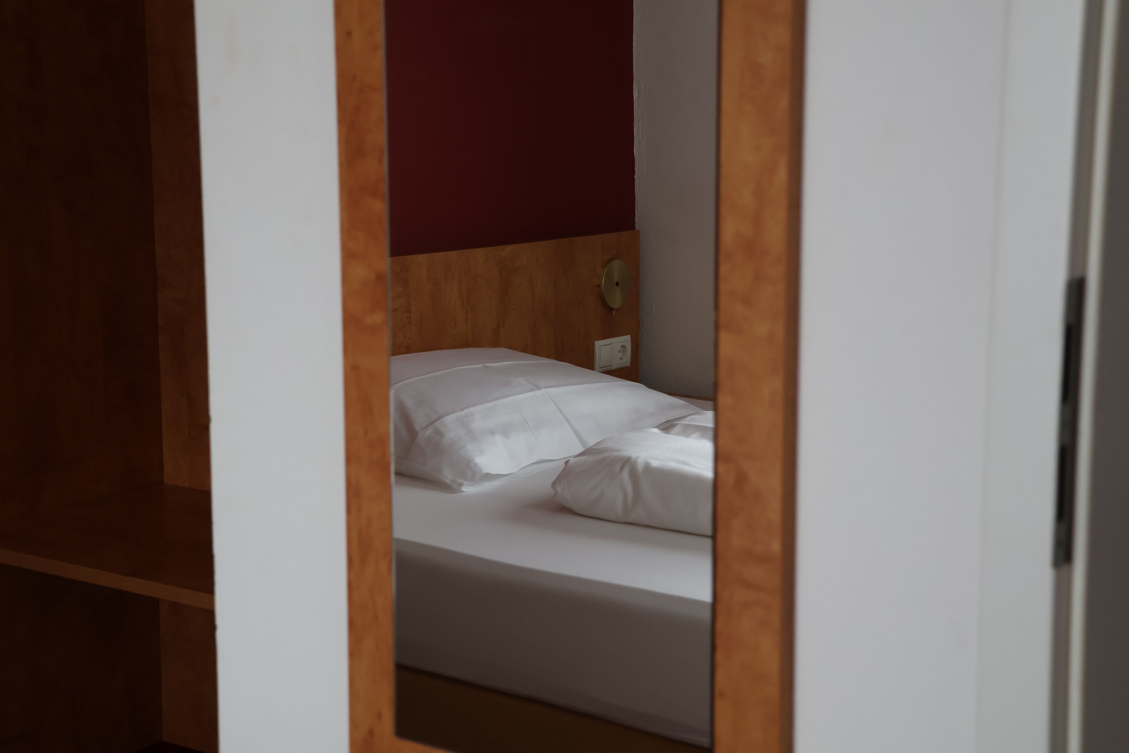 A single bed with white bedding in a room with wooden headboard and a red accent wall.
