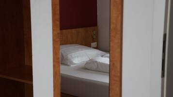 A single bed with white bedding in a room with wooden headboard and a red accent wall.