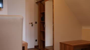A room with a wooden wardrobe, a small table, and a door leading to another room.