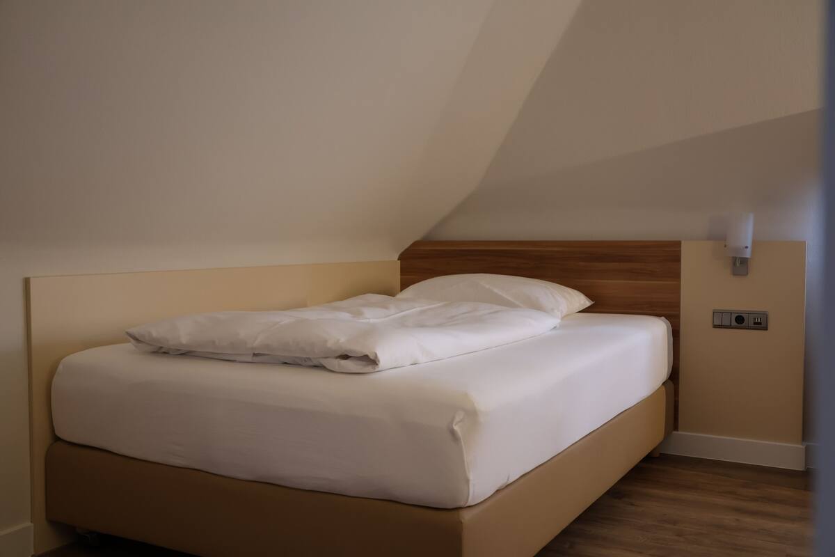 Een enkel bed met houten hoofdbord in een kamer met een schuine kap.