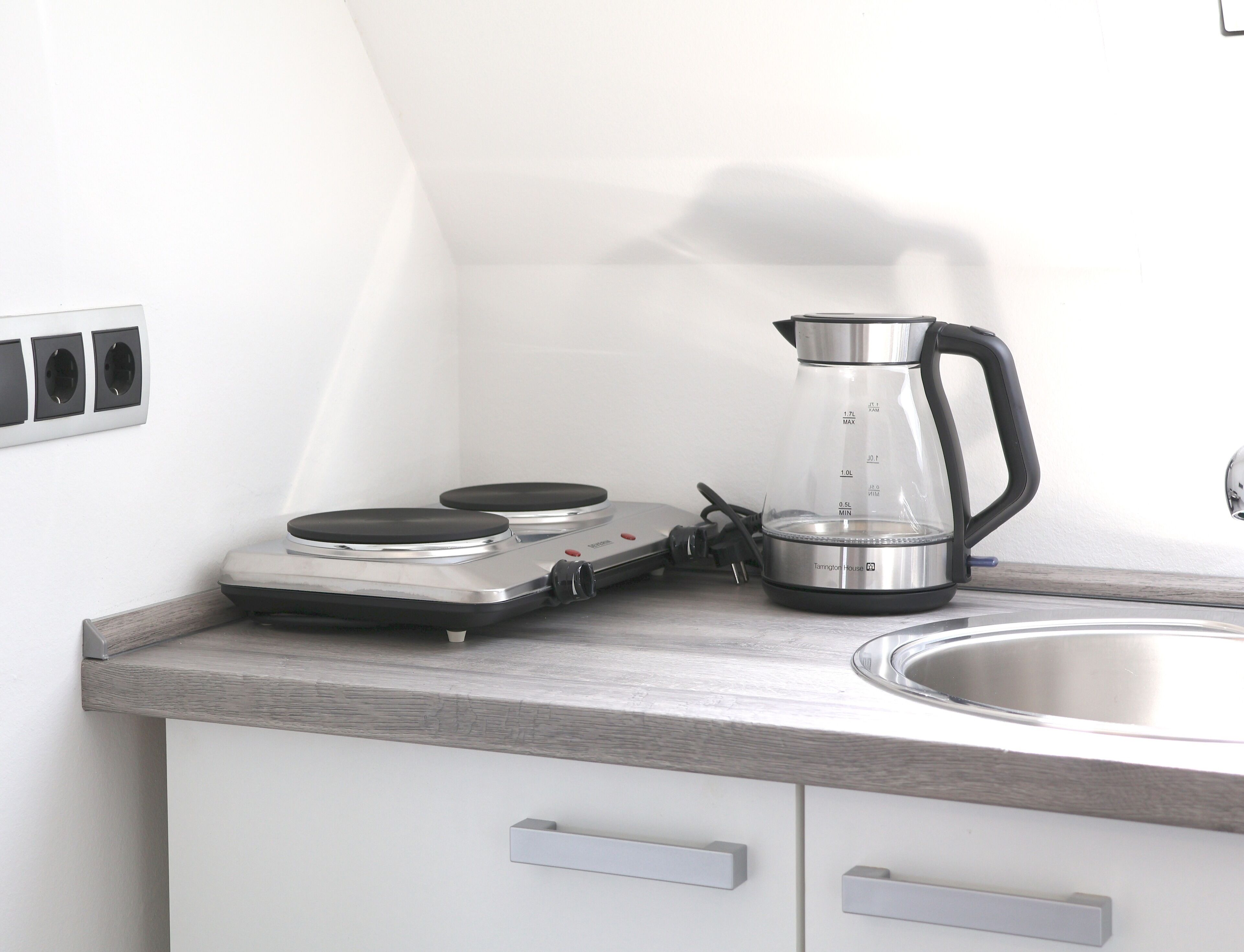 Una kitchenette con estufa, hervidor y lavamanos.