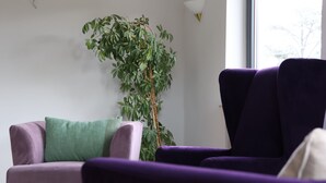 A room with a purple sofa, a green pillow, and a tall green plant. - Hotel an der Therme (Bad Durkheim)