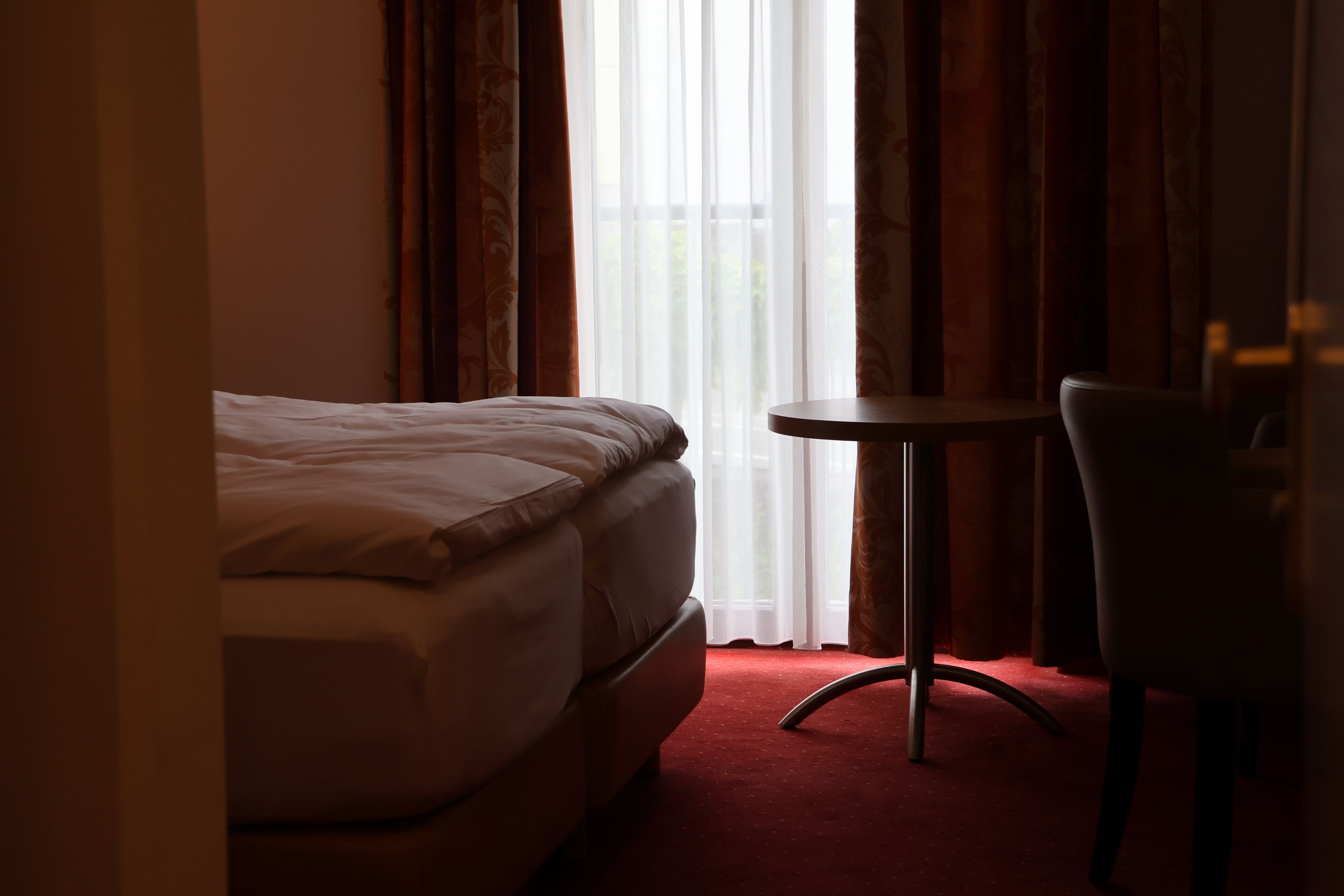 A hotel room with a bed, a small round table, and a chair.