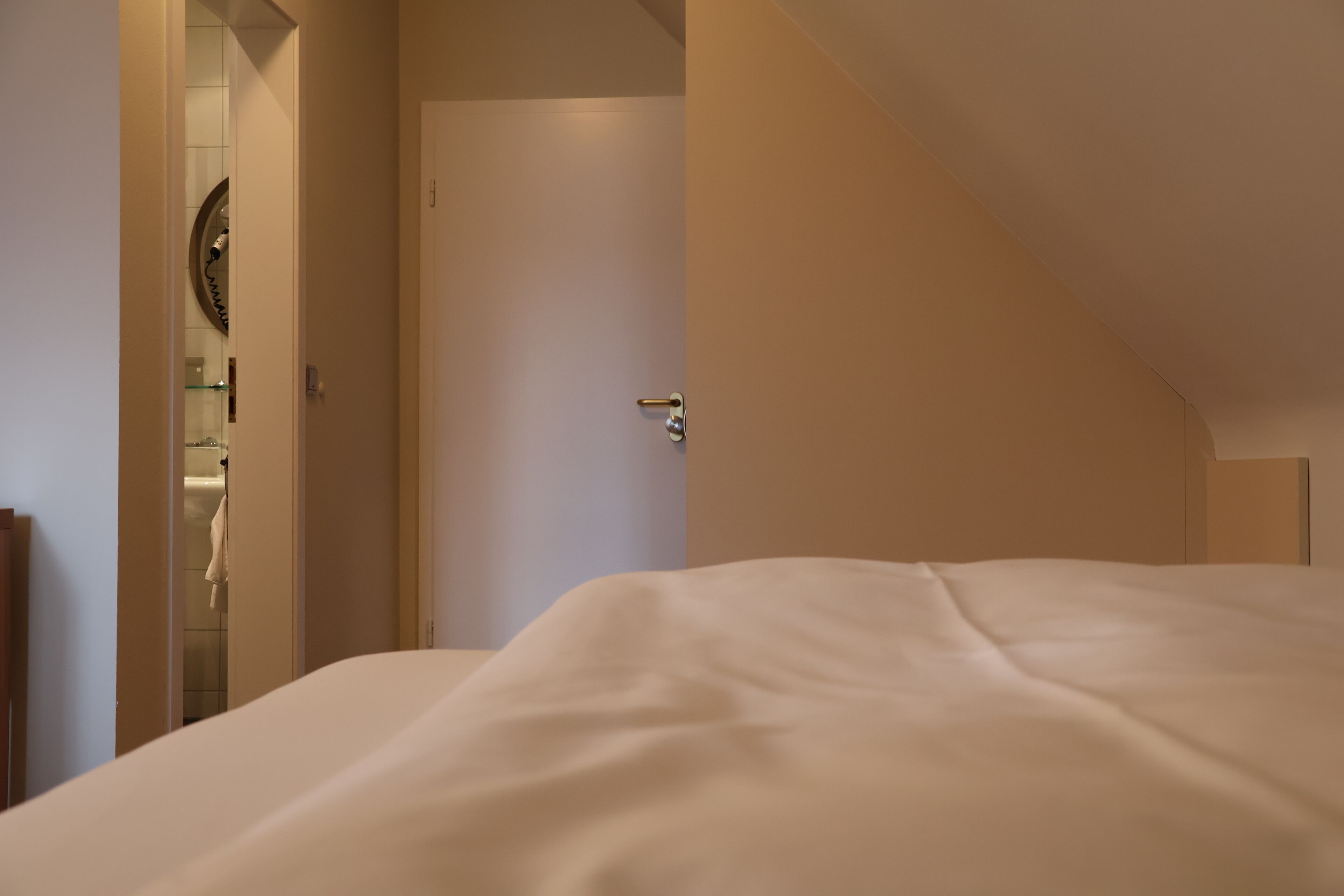A bedroom with a large bed, a door leading to a bathroom, and a small mirror on the wall.