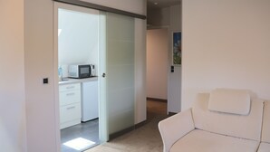 A modern interior with a white sofa, a kitchen area with a microwave, and a sliding door leading to another room. - Hotel an der Therme (Bad Durkheim)