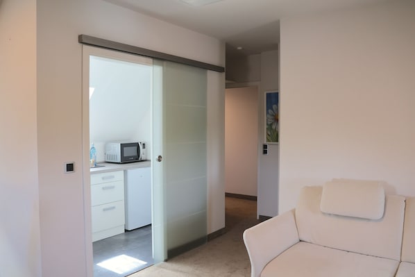 A modern interior with a white sofa, a kitchen area with a microwave, and a sliding door leading to another room. - Hotel an der Therme (Bad Durkheim)