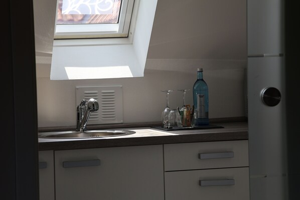A kitchen with a window above the sink, a bottle of blue liquid, and a wine glass on the counter. - Hotel an der Therme (Bad Durkheim)