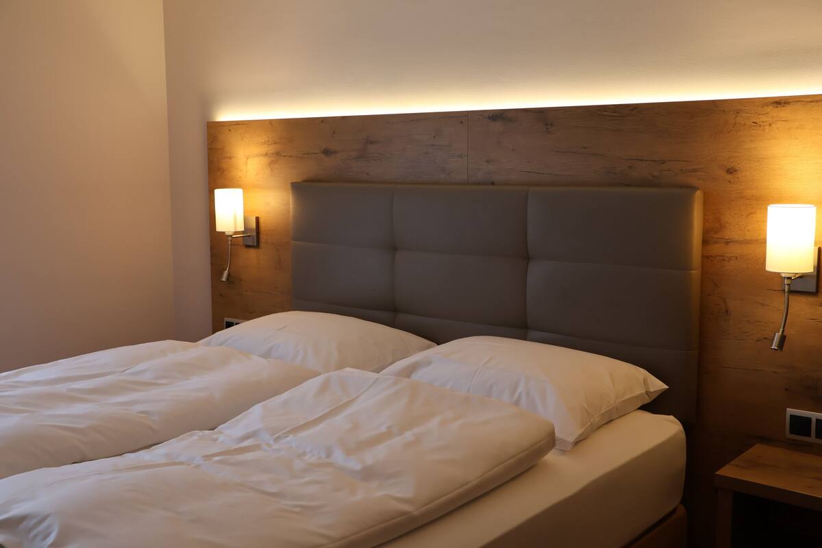 Een tweepersoonsbed met een houten hoofdbord, twee bedlampen en een nachtkastje.