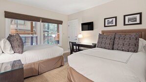 Une chambre d’hôtel avec deux lits, un bureau, une chaise, une télévision et une fenêtre avec des stores.