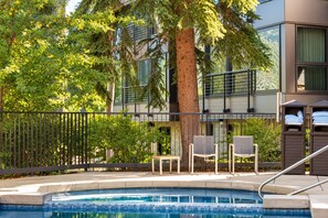 A swimming pool with chairs and a tree, surrounded by a fence.