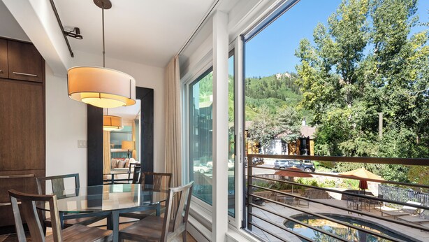 Un espace repas moderne avec une table et des chaises en verre, de grandes fenêtres donnant sur une piscine et un coin salon extérieur.