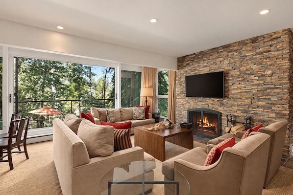 A modern living room with a stone fireplace, comfortable seating, and a large window overlooking greenery.