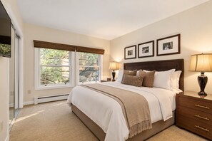 A bedroom with a large bed, bedside lamps, a nightstand, and framed pictures on the wall.