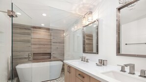 Une salle de bain moderne avec une baignoire sur pieds, un grand miroir et un meuble-lavabo blanc.
