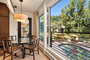 A modern dining area with a glass table and chairs, a large window with a view of a pool and greenery, and a cozy seating area with a lamp.