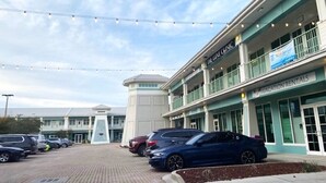 A building with a sign for 'The Luxury Clinic' and 'Vacation Rentals'. There are parked cars in front. - Dances with Waves - Villagio C245 Condo in Beautiful Perdido Key, FL (Pensacola)