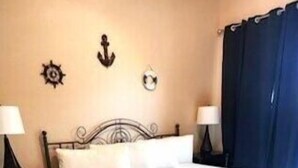 A bedroom with a wooden floor, a bed with white bedding, two bedside tables with lamps, and a blue curtain. - Dances with Waves - Villagio C245 Condo in Beautiful Perdido Key, FL (Pensacola)