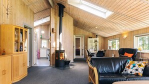 L’intérieur chaleureux d’un chalet comprend un poêle à bois central, un coin repas avec une table et des chaises, et un salon avec un canapé et une table basse.