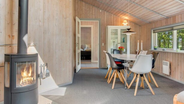 Une pièce chaleureuse avec un poêle à bois, une table à manger avec des chaises et une fenêtre donnant sur les arbres.