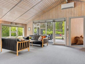 A modern interior with a wooden ceiling, a black leather sofa, a wooden chair, and a glass door leading outside. - 6 Person Holiday Home in Saeby (Sæby)