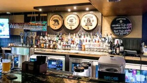 Zona de bar con varias botellas de licor, un grifo de cerveza y un panel con la carta de precios.