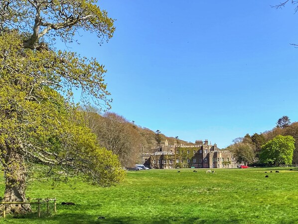 A large, historic building with multiple chimneys and a well-maintained lawn in the foreground.