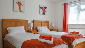 A hotel room with two wooden beds, white linens, orange towels, and artwork on the walls. - Escape to Barnhayes, a charming retreat in the picturesque village of Hartland. (Hartland)