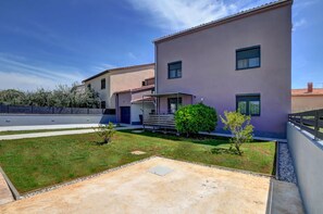 A modern two-story building with a flat roof, a covered outdoor seating area, and a small garden with a lawn and a few shrubs. - Lovely Relaxing Studio With Terrace (Fazana)