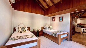 Una habitación con dos camas de madera, ropa de cama blanca y una cocina visible a través de un arco.