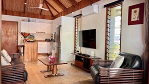 Una sala de estar moderna con techo de madera, televisor, sofá, una mesa de centro y un área de cocina al fondo.