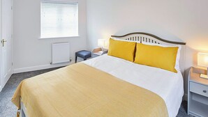 Une chambre d’hôtel comprenant un lit, une table de chevet, une lampe, une fenêtre avec des stores, un radiateur et un luminaire suspendu.