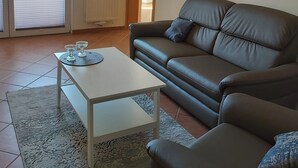 Un salón con una mesa de centro blanca, un sofá de cuero marrón y un ventanal con vistas a zonas verdes.