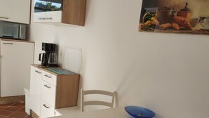 Una cocina con una mesa blanca, sillas, cafetera y un cuadro en la pared.