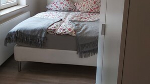 Un dormitorio con cama, almohadas, una manta, una ventana y un radiador.