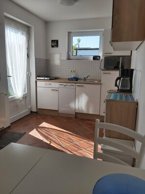 A compact kitchen with white cabinets, a tiled backsplash, a window, and a coffee maker.