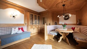 A cozy room with wooden walls and ceiling, a blue sofa with red cushions, a wooden bench, and a small table with a vase of flowers. - Spacious vacation apartment in Kaiserwinkl - perfect for the whole family (Kössen)