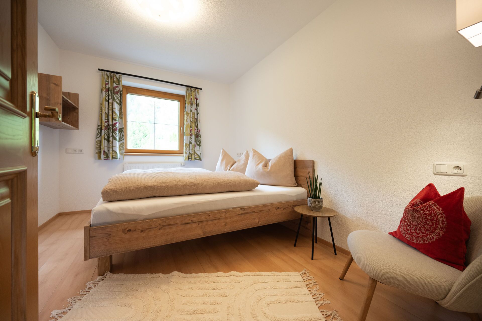 A bedroom with a bed, a chair, a small table, and a window with curtains.