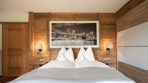 A hotel room with a wooden headboard, a large framed cityscape picture, two bedside lamps, and a bed with white bedding. - Spacious vacation apartment in Kaiserwinkl - perfect for the whole family (Kössen)
