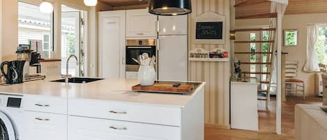 A modern kitchen with white cabinetry, a built-in washing machine, and a dining area with a wooden table.